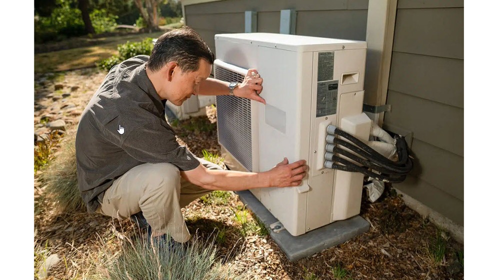 Technician working at a heat pump unit alongside a single family residence